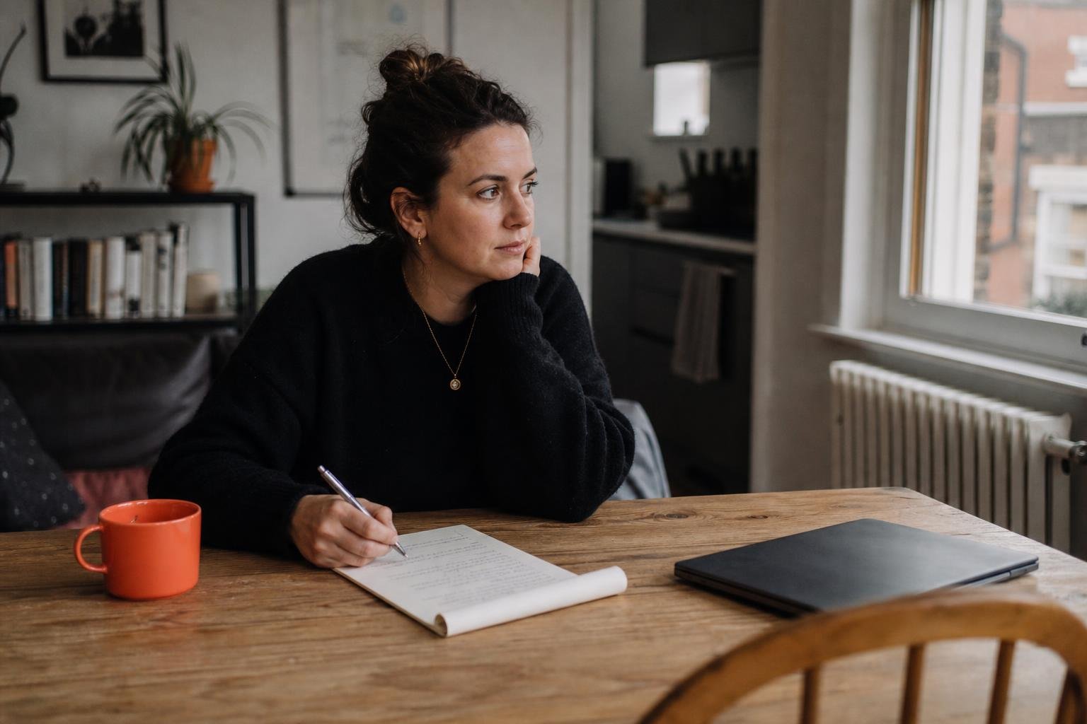 A woman at a kitchen table with a notepad, drawing up a shortlist of PPC agencies for SaaS