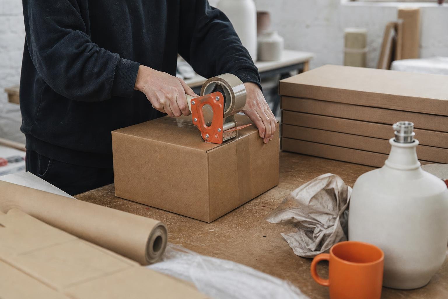 Maker taping a boxed ceramic lamp base in a small British workshop, the kind of brand weighing up PPC agency costs